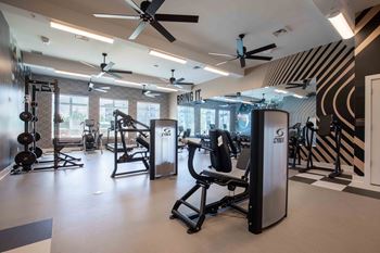 A gym with cardio machines and other equipment in a room with windows